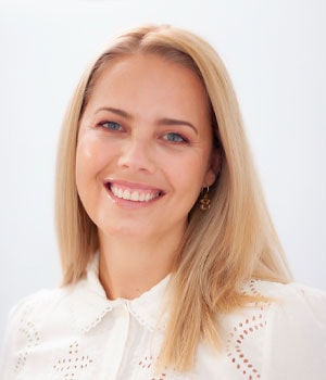 Una mujer de largo cabello rubio sonriendo, vestida con una blusa blanca con cuello. Para obtener más información o consultas, contactar con gehocan.