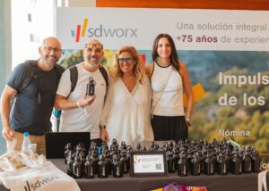 Cuatro personas de pie juntas detrás de una mesa cubierta de botellas de agua con la marca. Al fondo hay una pancarta con la palabra "sdworx" y un texto en español.