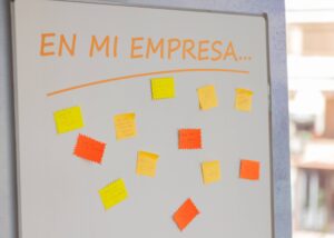 Pizarra blanca con "EN MI EMPRESA..." escrito en la parte superior, cubierta con notas adhesivas de colores que contienen mensajes escritos a mano.