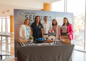 Un grupo de cinco personas detrás de una mesa promocional con folletos y artículos de marca.