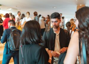 Un grupo de personas conversando en un evento social, con una persona sosteniendo una taza en primer plano.