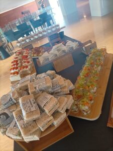 Una mesa de buffet con una variedad de sándwiches y aperitivos, incluyendo verduras en tazas y sándwiches tipo finger.