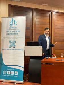 Persona dando una presentación cerca de una pancarta que dice "gehocan" en una habitación con paredes de madera.