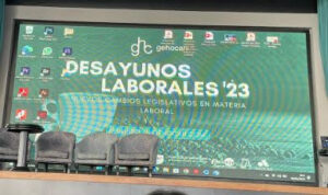 Escenario de conferencias con una pantalla grande que muestra "Desayunos Laborales '23: Nuevos Cambios Legislativos en Materia Laboral". Frente a la pantalla hay tres sillas vacías.