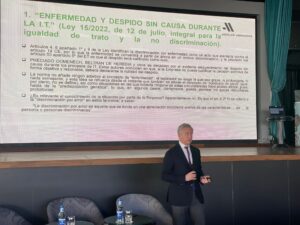Una persona da una presentación en una sala con una pantalla grande que muestra un texto en español sobre la legislación laboral (Ley 15/2022) en materia de discriminación e igualdad.