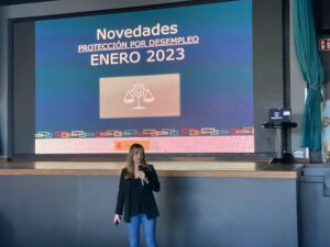 Una persona hablando frente a una presentación titulada "Novedades Protección por Desempleo Enero 2023" en un escenario.
