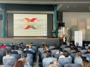 Una persona presenta una presentación de diapositivas en el escenario ante una audiencia en una sala de conferencias.