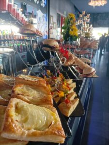 Una mesa de buffet con diversos pasteles, sándwiches y brochetas exhibidos en un entorno de restaurante.