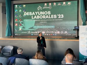 Una persona habla frente a un público en una presentación titulada "Desayunos Laborales '23" sobre cambios legislativos en materia laboral. Una gran pantalla muestra varios íconos y logotipos.