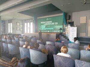 Personas asistiendo a una presentación en una sala de conferencias con una pantalla grande que muestra "Desayunos Laborales '23.