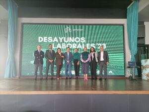 Siete personas están de pie en un escenario con una pancarta que dice "Desayunos Laborales '23" en el fondo.