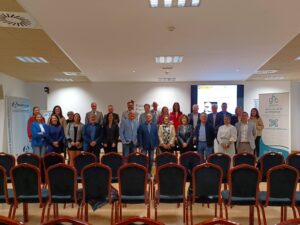 Un grupo de personas posando para una foto en una sala de conferencias con sillas vacías en primer plano y pancartas de fondo.