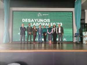 Siete personas se encuentran en el escenario frente a una gran pantalla en la que se muestra "Desayunos Laborales '23".