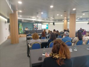 Personas sentadas en una sala de conferencias, escuchando un panel de discusión en la parte delantera.