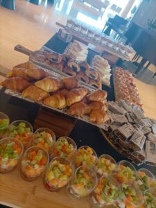 Una mesa de buffet con croissants, sándwiches, pasteles, copas de fruta y aperitivos dispuestos en filas.
