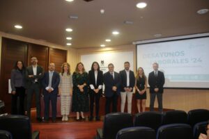 Un grupo de nueve personas están de pie en fila en una sala de conferencias, con una pantalla de presentación que muestra "Desayunos Laborales '24" detrás de ellos.