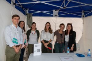 Seis personas sonriendo bajo una carpa en un stand con un cartel que dice "Ofertas de empleo".