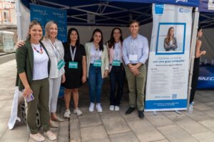 Un grupo de seis personas se encuentra frente a un stand debajo de una carpa azul con pancartas de marketing.
