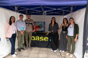 Grupo de siete personas de pie bajo una tienda de campaña, posando para una foto con una mesa y un monitor que muestra una imagen.
