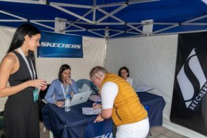 Personas en una cabina de registro bajo una carpa azul con la marca Skechers; una persona está firmando un documento.