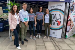 Un grupo de cinco personas paradas juntas en un evento frente a un stand que muestra una pancarta de "Koala Bay".