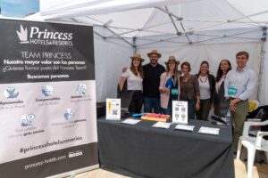 Un grupo de personas de pie en un stand de reclutamiento de Princess Hotels & Resorts bajo una carpa blanca con materiales promocionales sobre la mesa.
