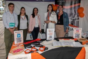 Un grupo de seis personas detrás de una mesa con materiales promocionales y códigos QR en un stand de eventos.