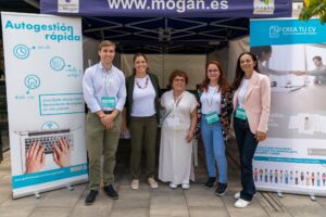 Cinco personas de pie frente a un stand con carteles relacionados con el trabajo, sonriendo a la cámara. Llevan acreditaciones de la conferencia.
