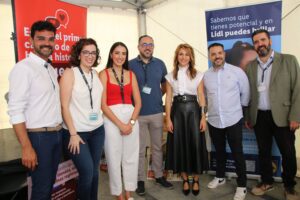 Siete personas paradas juntas frente a carteles promocionales, sonriendo para una foto grupal.