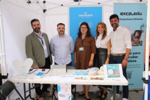 Un grupo de cinco personas está detrás de una mesa con folletos y una computadora portátil debajo de una carpa blanca en un evento.