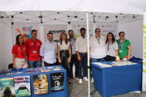 Un grupo de personas se encuentra dentro de un stand blanco con materiales educativos sobre mesas. Se exhiben carteles y pancartas de la organización Don Bosco.