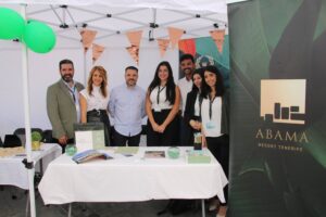 Grupo de personas detrás de un stand bajo un toldo. El stand muestra material promocional de Abama Resort Tenerife.