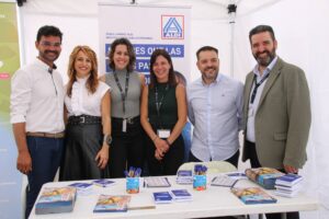 Seis personas de pie detrás de una mesa con materiales y bolígrafos de la marca ALDI, sonriendo para una foto grupal dentro de una carpa.