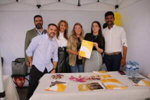 Grupo de seis personas de pie bajo un dosel, posando para una foto con materiales promocionales en una mesa frente a ellos.