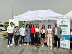 Un grupo de personas de pie frente a una carpa blanca y pancartas, sonriendo a la cámara.