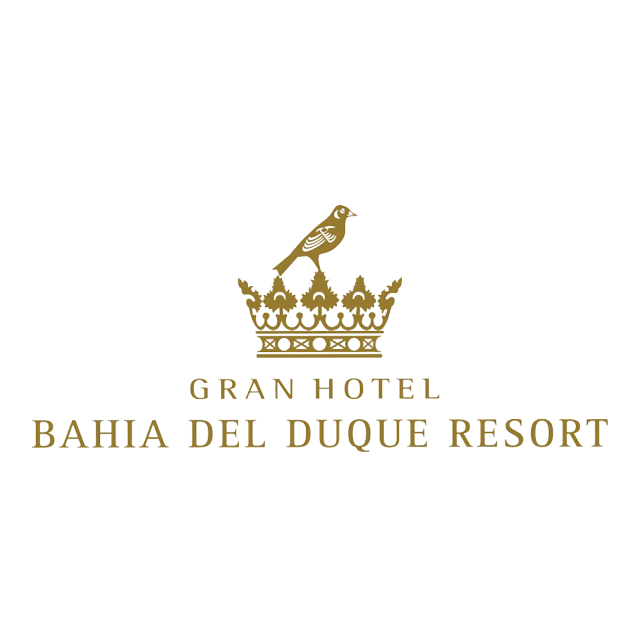 Logotipo del Gran Hotel Bahía Del Duque Resort, que presenta una corona dorada con un pájaro posado en la parte superior y el nombre del resort en letras mayúsculas doradas debajo.